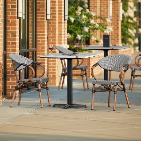 A Lancaster Table & Seating Versilla table with 2 French Bistro chairs on a patio.