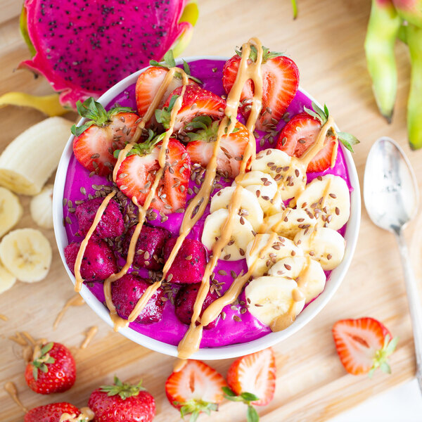 A bowl of Pitaya Foods organic dragon fruit cubes with strawberries and bananas on a table.