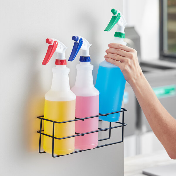 A person using a Lavex 3 compartment wall-mount holder for spray bottles.