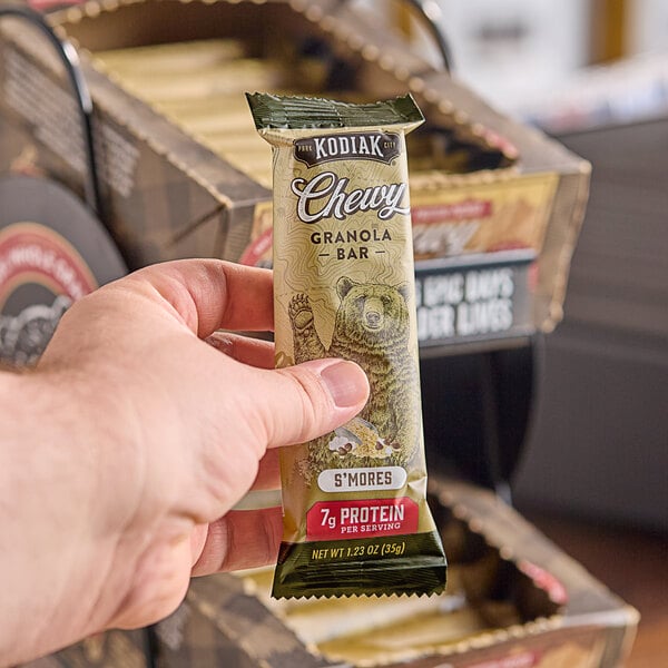 A hand holding a package of Kodiak Cakes S'mores Chewy Granola Bars.
