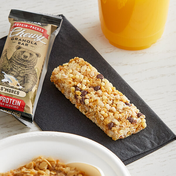 A Kodiak Cakes S'mores chewy granola bar on a table next to a cup of coffee and orange juice.