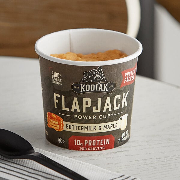 A cup of Kodiak Cakes Buttermilk and Maple Flapjack mix on a table with a spoon.