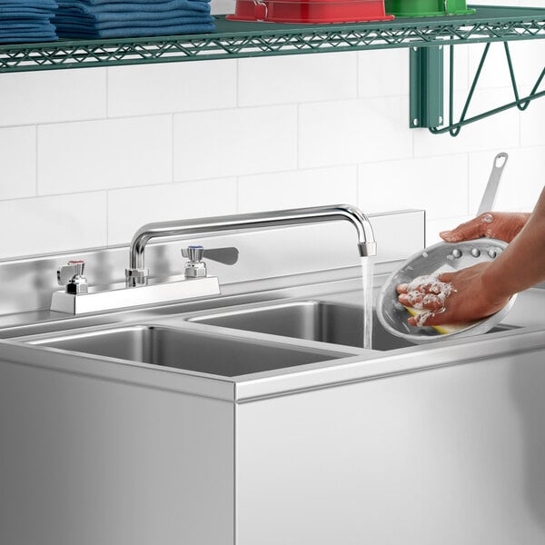 A person washing dishes in a stainless steel sink using a Regency deck-mounted faucet.