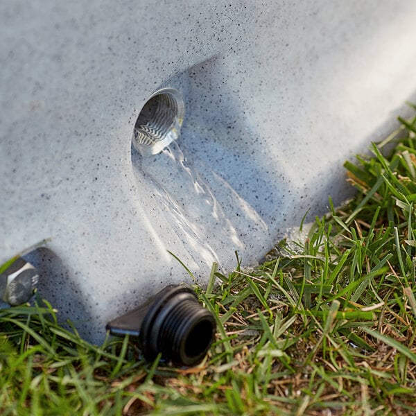 A water hose pouring into a concrete drain.