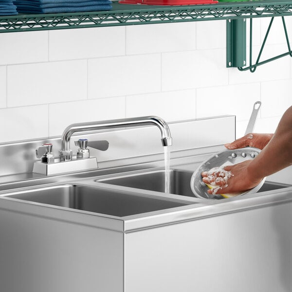 A person washing dishes in a stainless steel sink using a Regency deck-mounted faucet.