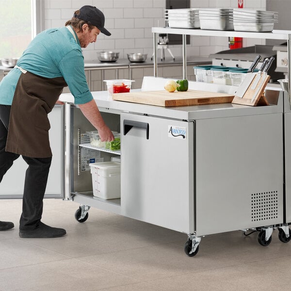 An aproned man using an Avantco worktop refrigerator in a kitchen.