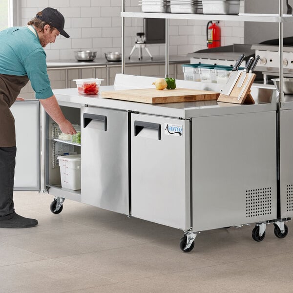 A man opening an Avantco worktop refrigerator in a kitchen.