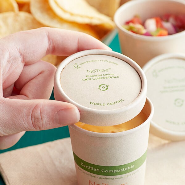 A hand holding a World Centric compostable paper hot cup lid over a cup of food.