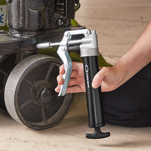 A hand using a Core Gear mini pistol grip grease gun to dispense grease.