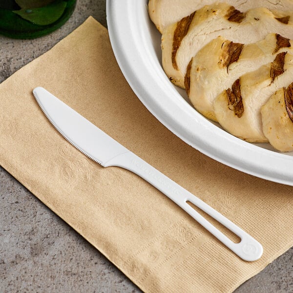 A white knife next to a plate of sliced chicken.