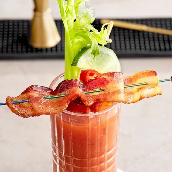 A glass of liquid with bacon on the rim.