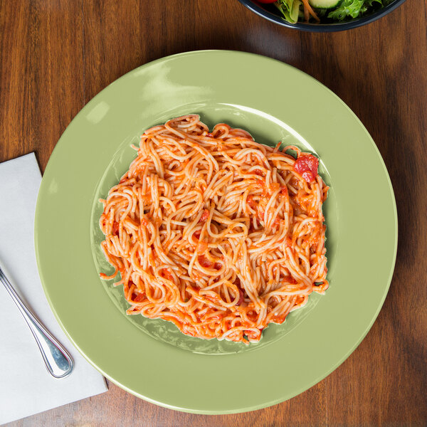 A plate of spaghetti and a Diamond Harvest avocado melamine bowl of salad on a table.