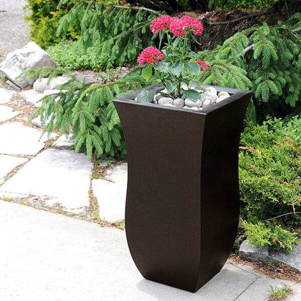A black Mayne Valencia planter with a plant in it on an outdoor patio table.
