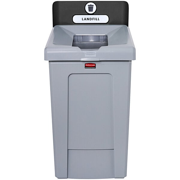 A grey plastic trash can with a black lid.