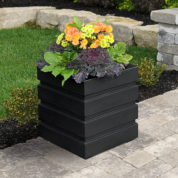 A Mayne black planter with colorful flowers on an outdoor table.