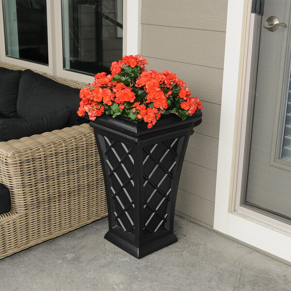 A black Mayne Georgian planter with orange flowers on an outdoor patio table.