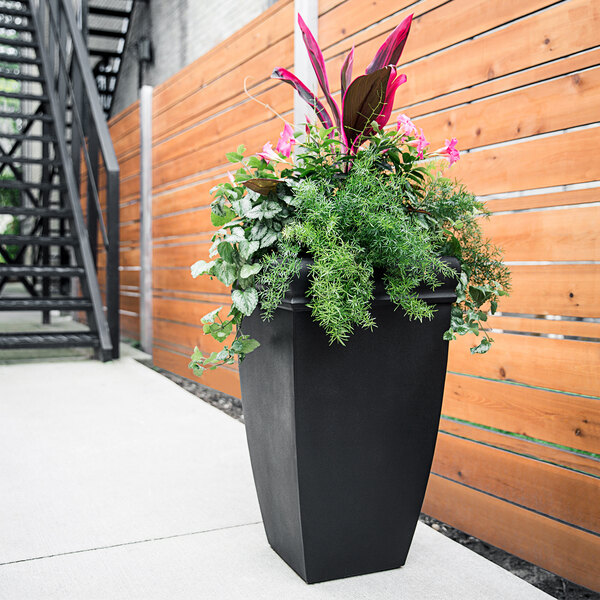 A black Mayne Chelsey planter with flowers and leaves.