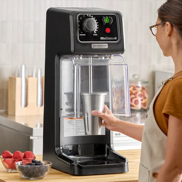 A woman using a Hamilton Beach heavy-duty drink mixer on a counter to make a smoothie.