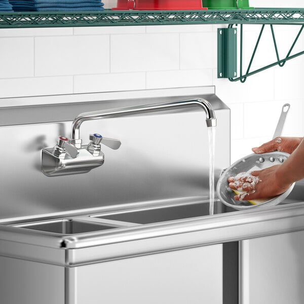 A person washing dishes in a sink with a Regency wall mount faucet running.