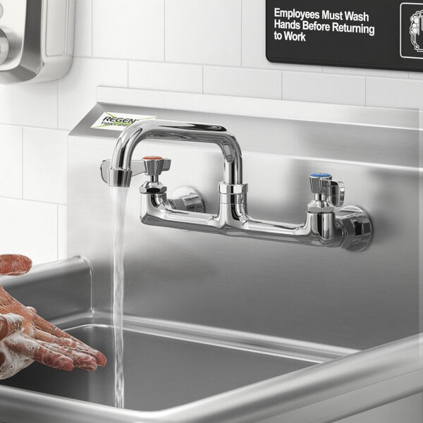 A person washing their hands under a Regency wall mount faucet.