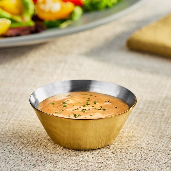 An American Metalcraft stainless steel sauce cup filled with sauce on a table in a salad bar.