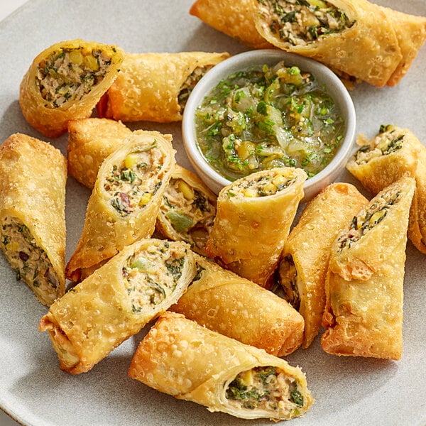 A plate of fried Southwest Chicken Egg Rolls with a small bowl of sauce.