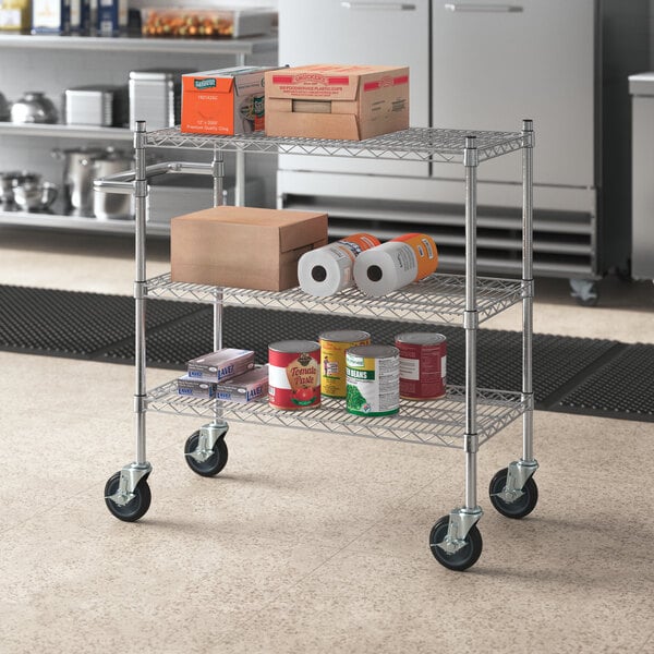 A chrome three shelf utility cart with food items on it.