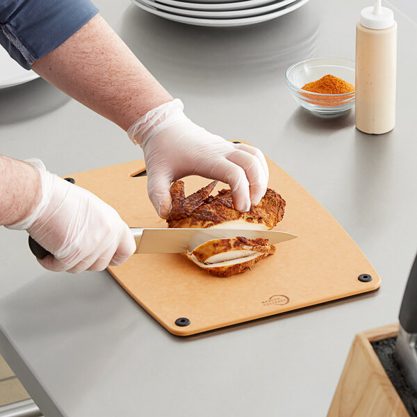A person cutting a chicken on a Mercer composite cutting board.