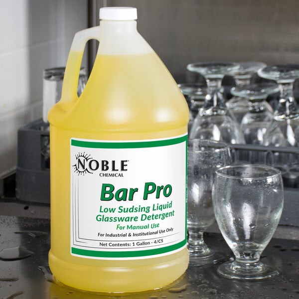 A bottle of Noble Chemical Bar Pro detergent on a bar counter next to a glass.