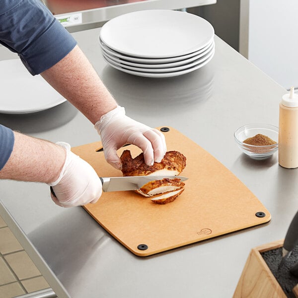 A person cutting a piece of chicken on a Mercer composite cutting board.