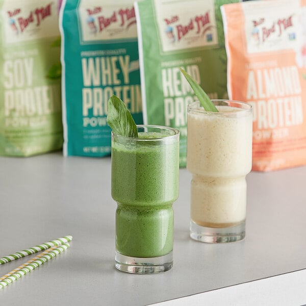 Two glasses of green and white Bob's Red Mill Gluten-Free Almond Protein smoothies on a table with a green leaf.