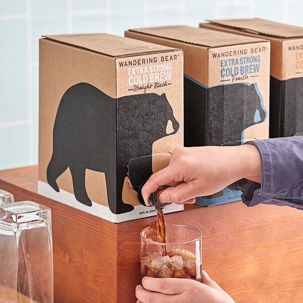 A person pouring Wandering Bear organic straight black cold brew coffee from a box into a glass.