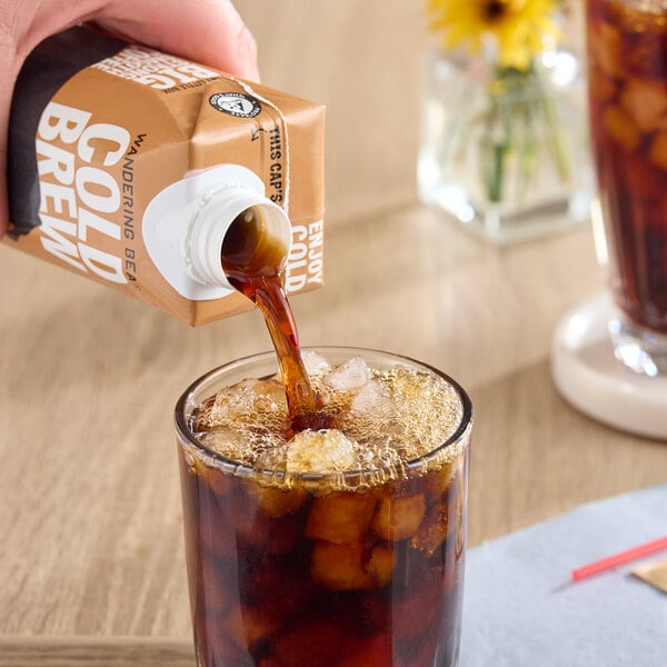 A carton of Wandering Bear Organic Straight Black Cold Brew Coffee being poured over ice into a glass.