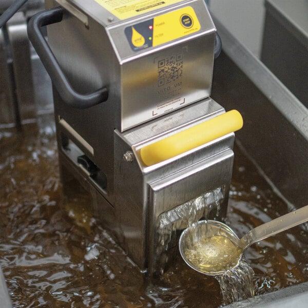 A VITO fryer oil filtration machine on a school kitchen counter being used to filter oil with a ladle.