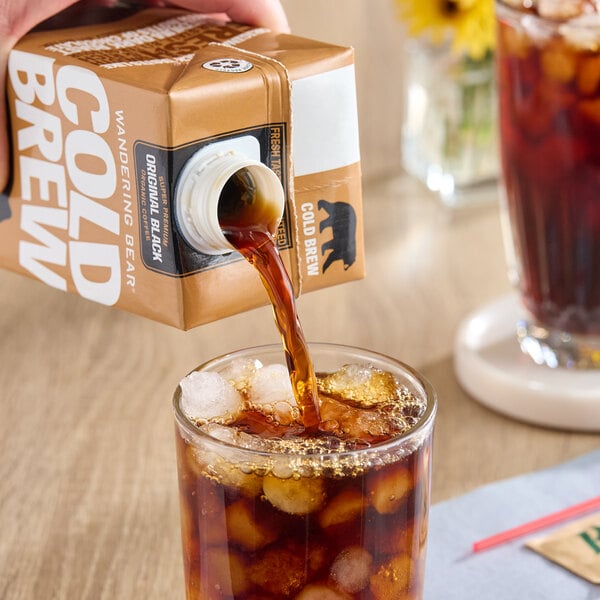 A carton of Wandering Bear Organic Straight Black Cold Brew Coffee being poured over ice into a glass.
