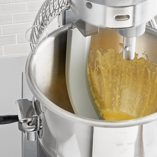 An Avantco mixing bowl with yellow liquid in it, using a bowl scraper attachment.