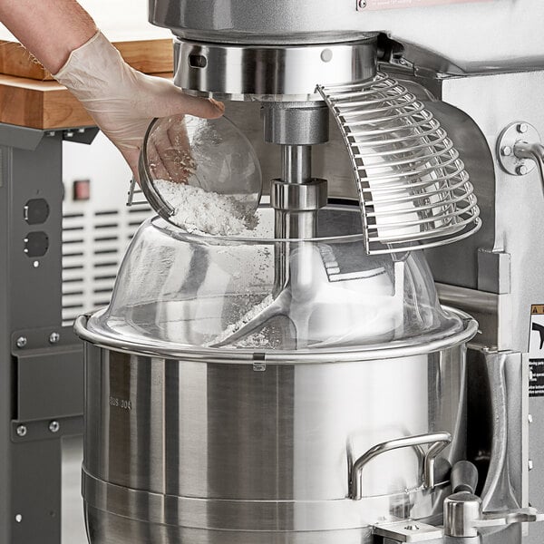 A person uses an Avantco mixer with a splash cover to mix flour in a bowl.