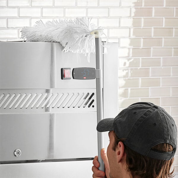 A person using a Lavex angled duster with a white pole to dust a stove.