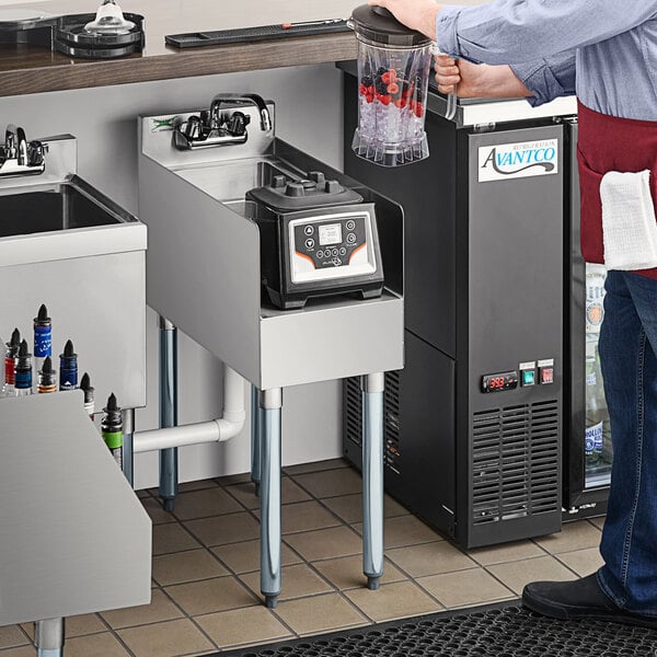 A person standing next to a Regency stainless steel blender station with sink and faucet.