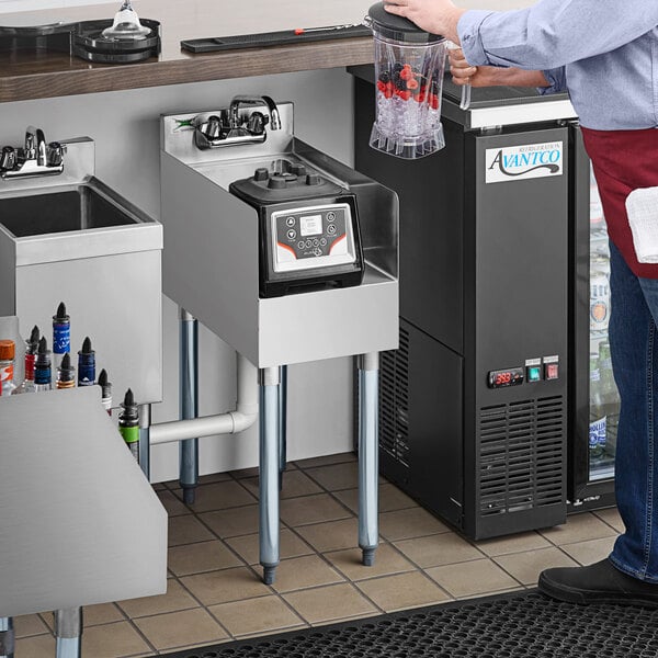 A man standing at a stainless steel Regency blender station with a drink.