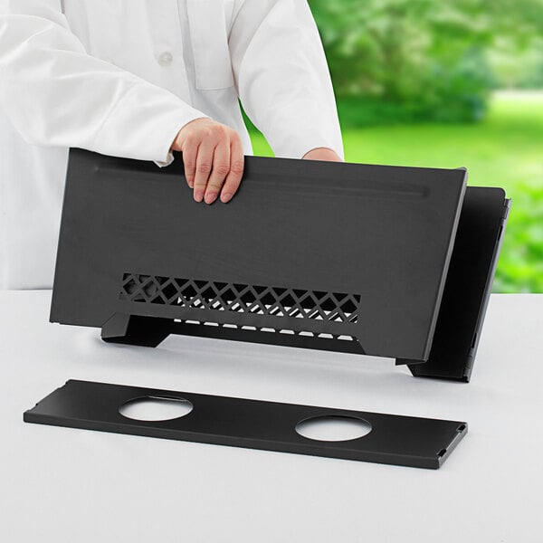 A person holding a black rectangular Chef Master wind guard.