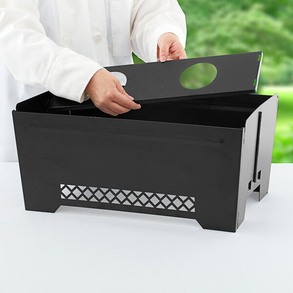 A person opening a black metal box with the Chef Master Collapsible Chafer Wind Guard inside.
