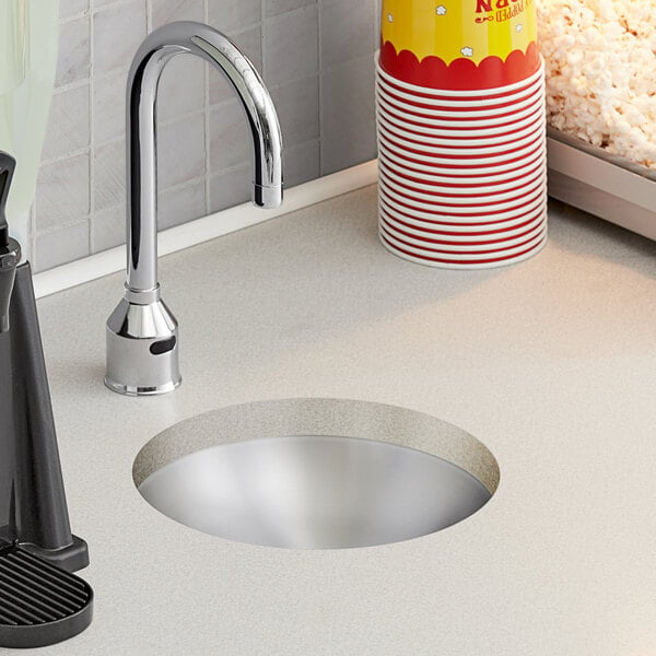 A close-up of a Regency round undermount sink with a cup of soda and popcorn on the counter.