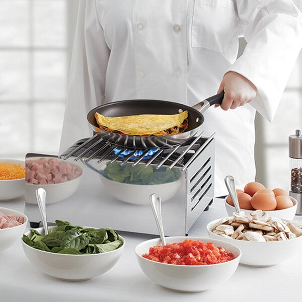 A chef cooking food on a Chef Master stainless steel butane stove cover over a pan.