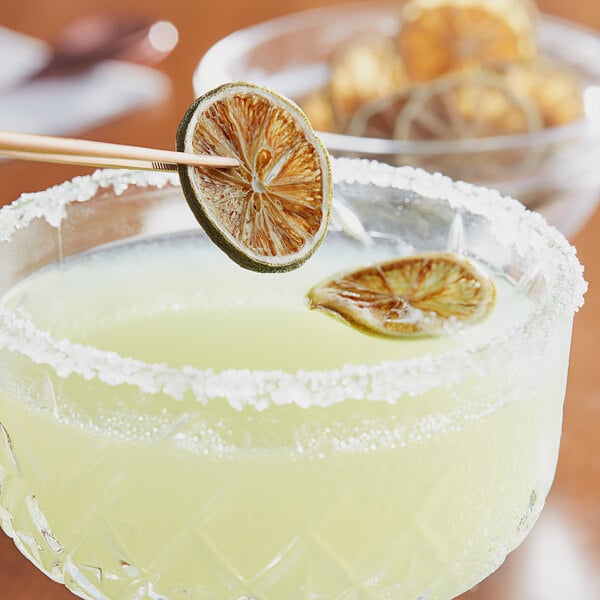 Dried key lime slices on a wooden stick garnishing a cocktail.