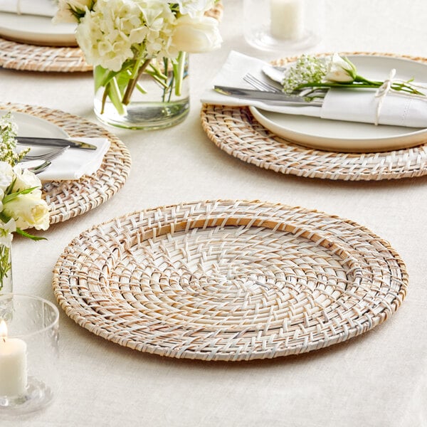 A table set with Acopa blond rattan charger plates, white plates, and white flowers.