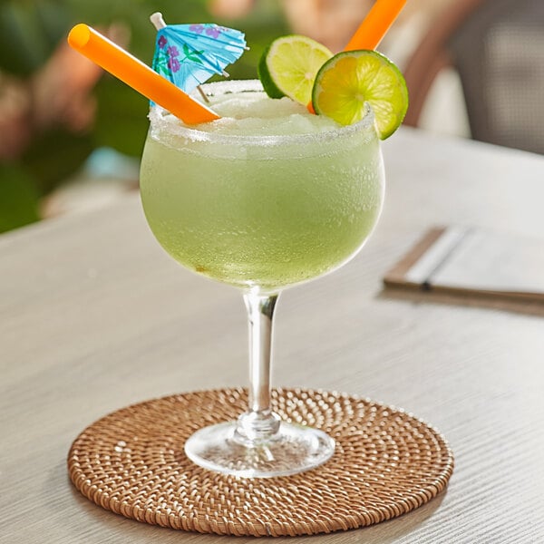 A Acopa gin and tonic glass filled with a green drink with orange and lime straws.