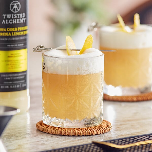 Two glasses of yellow liquid with lemon garnishes on a table.