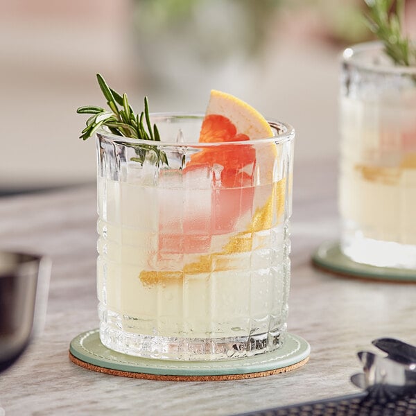 A glass of Twisted Alchemy grapefruit cocktail with ice, an orange slice, and rosemary.