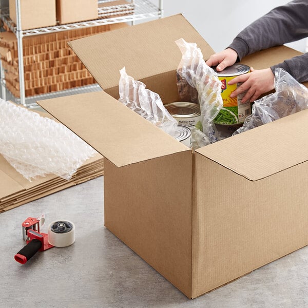 A hand packing a yellow container of food in a Lavex shipping box.